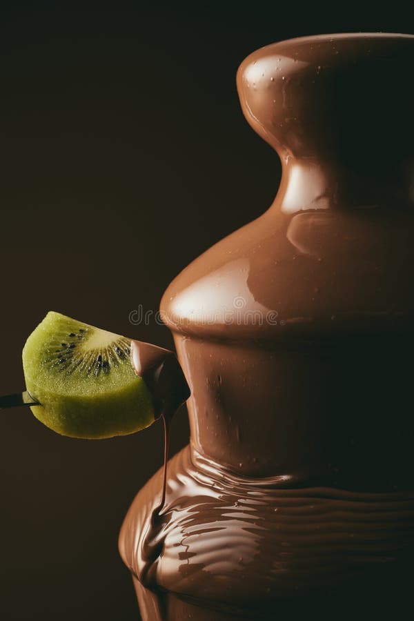 Persona anonima che immerge kiwi nel cioccolato immagine stock