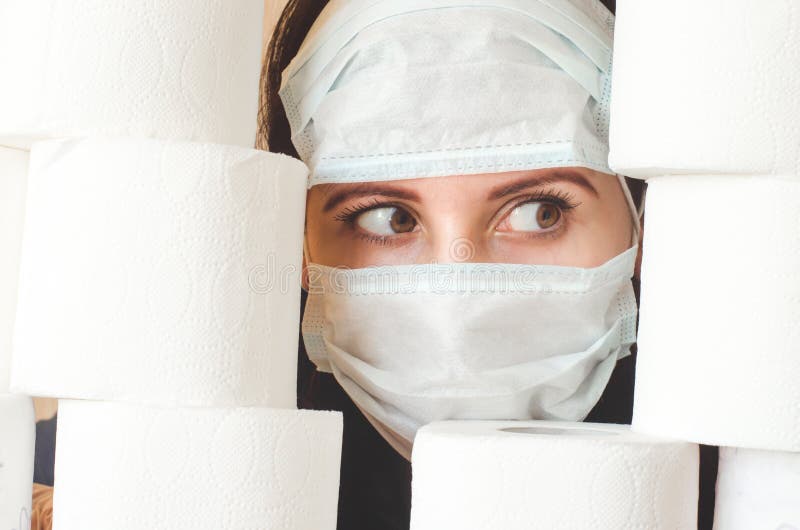 Persona asustada en dos máscaras faciales de protección contra virus médicos mira a través de pilas de papel higiénico. covid19 cu fotos de archivo