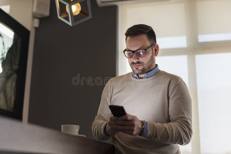 Handsome man standing next to a counter in restaurant, typing a text message using smart phone. Handsome man standing next to a counter in restaurant, typing a text message using smart phone