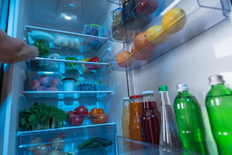 Persona che raggiunge in un frigorifero per alimento fresco fotografia stock Persona che raggiunge in un frigorifero per alimento fresco fotografia stock