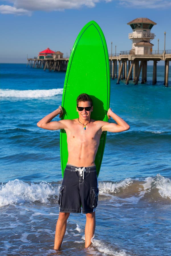 Persona que practica surf adolescente del muchacho que sostiene la tabla hawaiana en la playa imagen de archivo libre de regalías Persona que practica surf adolescente del muchacho que sostiene la tabla hawaiana en la playa imagen de archivo libre de regalías