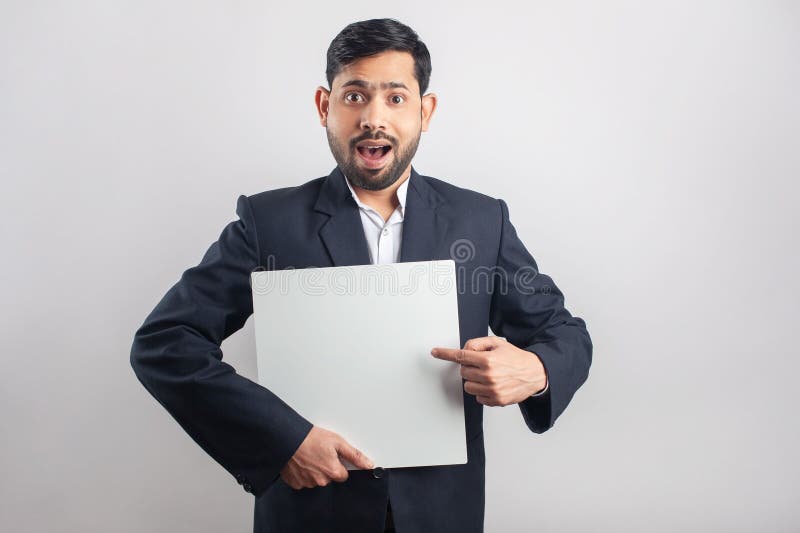 formal dressed indian man pointing finger towards blank placard with surprised expression. formal dressed indian man pointing finger towards blank placard with surprised expression