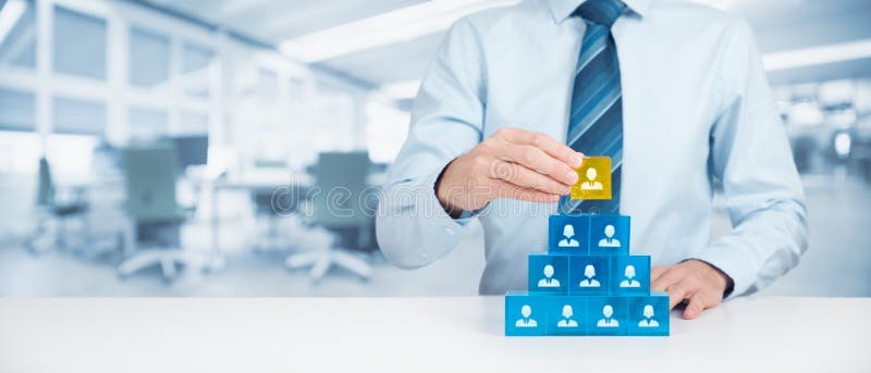 Human resources and corporate hierarchy concept - recruiter complete team by one leader person (CEO) represented by gold cube and icon. Wide banner composition with office in background. Human resources and corporate hierarchy concept - recruiter complete team by one leader person (CEO) represented by gold cube and icon. Wide banner composition with office in background.