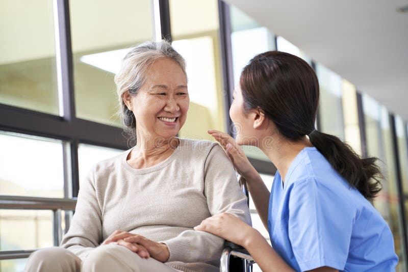 Friendly caregiver of nursing home talking to asian senior woman in hallway. Friendly caregiver of nursing home talking to asian senior woman in hallway