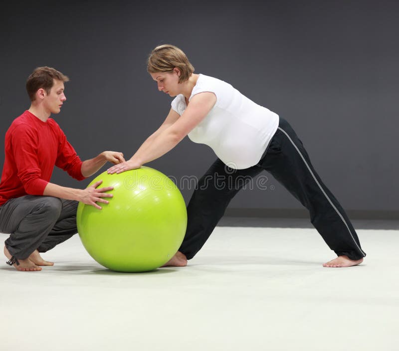 Serious caucasian pregnant women exercising with personal trainer on large stability ball in studio. Serious caucasian pregnant women exercising with personal trainer on large stability ball in studio