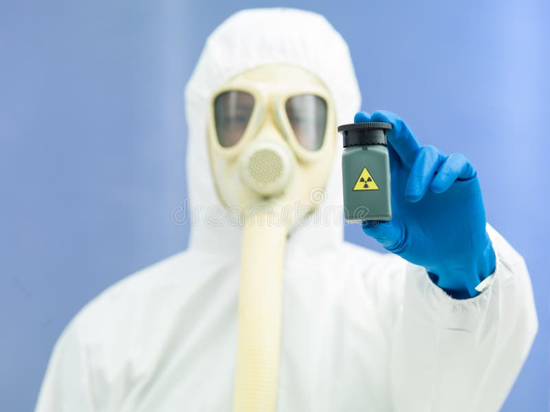 Person in bio hazard suit and gas mask holding a radioactive isotope sample in a small green plastic jar. Person in bio hazard suit and gas mask holding a radioactive isotope sample in a small green plastic jar