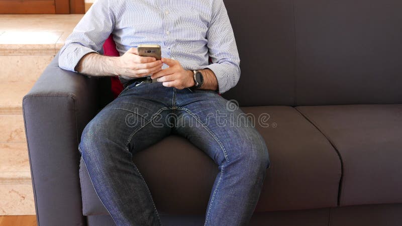 Personne dans les jeans et smartphone utilise chemise assis sur le sofa