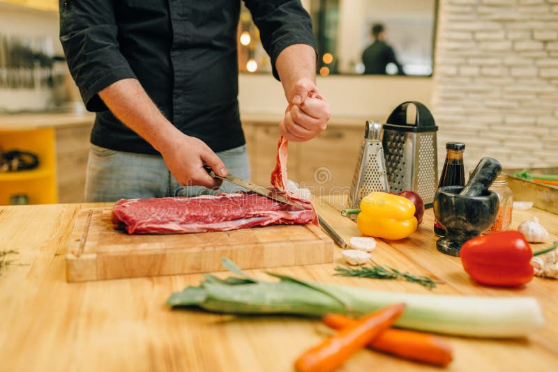 Personne masculine avec de la viande crue de coupes de couteau ? bord photos stock Personne masculine avec de la viande crue de coupes de couteau ? bord photos stock