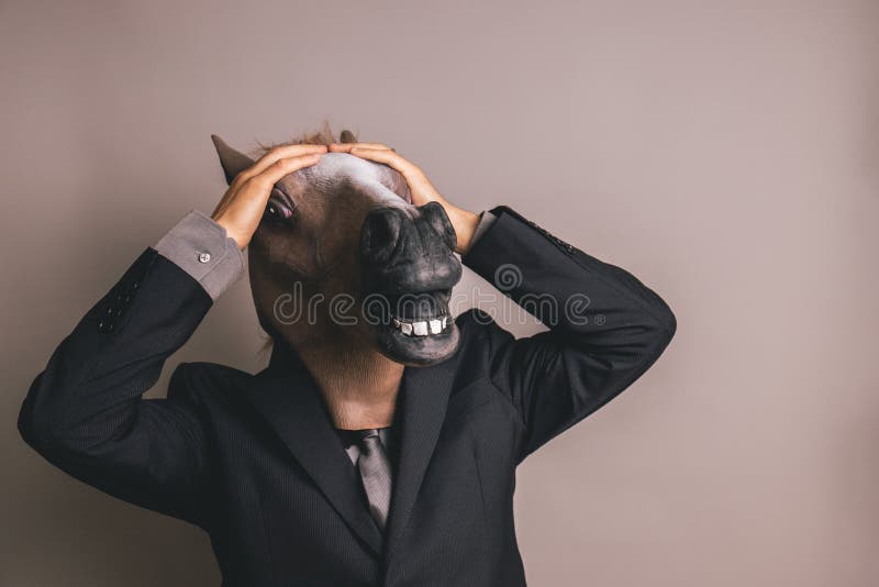 Personne non identifiée avec un costume et un lien gris-foncé portant un masque de cheval avec les deux mains sur la tête photos stock Personne non identifiée avec un costume et un lien gris-foncé portant un masque de cheval avec les deux mains sur la tête photos stock