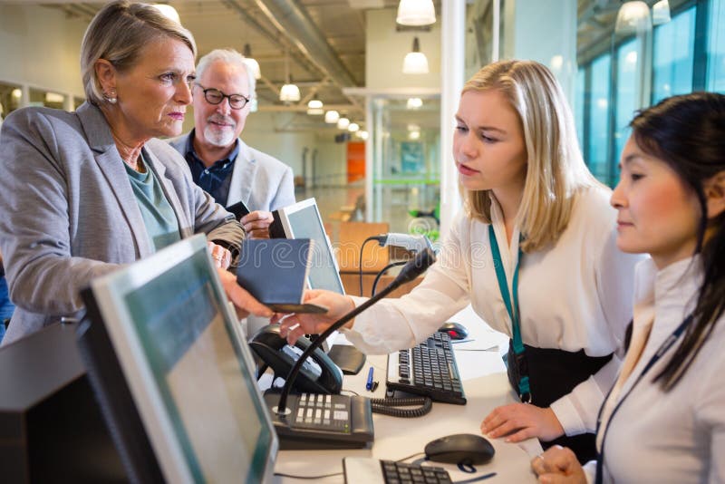 Female staff members looking at passport held by businesswoman at airport check-in. Female staff members looking at passport held by businesswoman at airport check-in