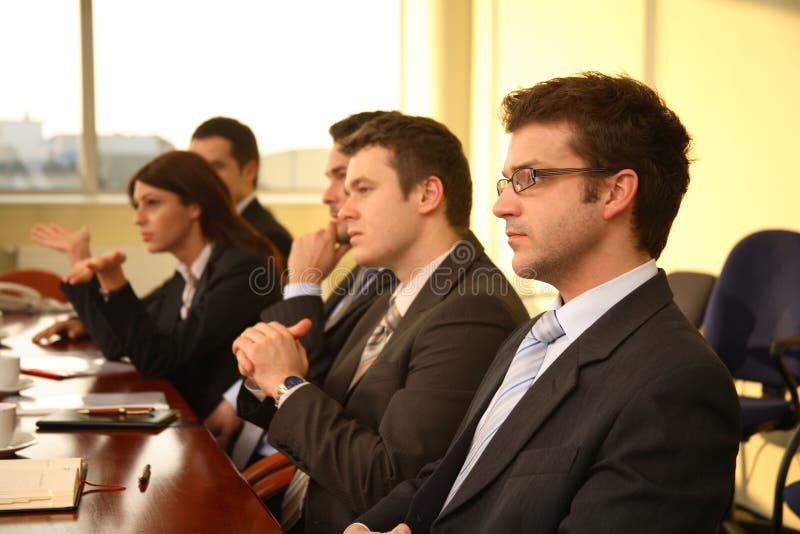 Five business persons in suits sitting at a conference table, taking part in a meeting and/or presentation. Five business persons in suits sitting at a conference table, taking part in a meeting and/or presentation.