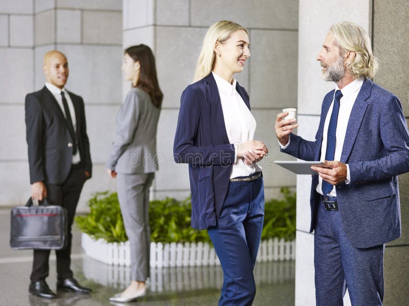 Personnes d'entreprise multinationales se tenant parlantes dans le lobby du mode photos stock Personnes d'entreprise multinationales se tenant parlantes dans le lobby du mode photos stock