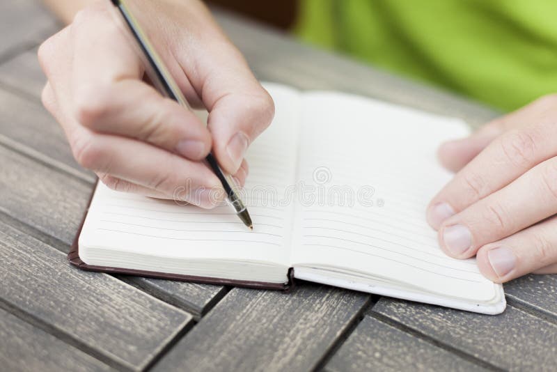 Young man writing notes on a notebook with a pen, close-up view of hands. Young man writing notes on a notebook with a pen, close-up view of hands