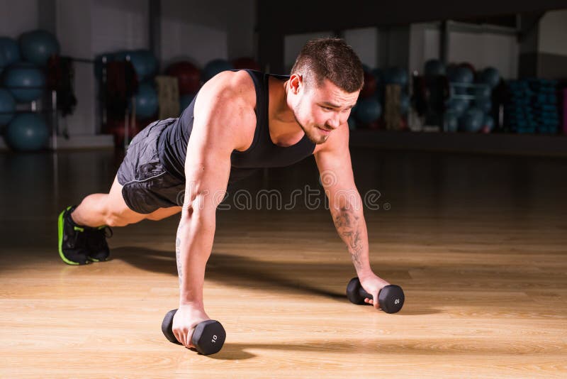 Pesas de gimnasia de Doing Pushups With del atleta del hombre joven como parte del entrenamiento del levantamiento de pesas fotos de archivo Pesas de gimnasia de Doing Pushups With del atleta del hombre joven como parte del entrenamiento del levantamiento de pesas fotos de archivo