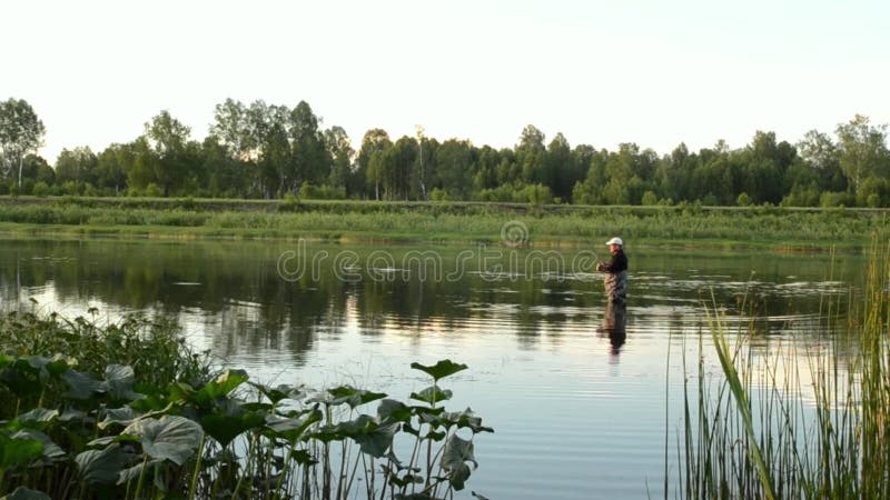 Pesca del pescador en un río tranquilo por la mañana Hombre en las artes de pesca stending en un río y tiros trole