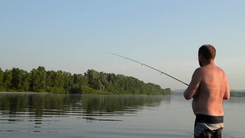 Pesca del pescador en un río tranquilo por la mañana Hombre en las artes de pesca stending en un río y tiros trole