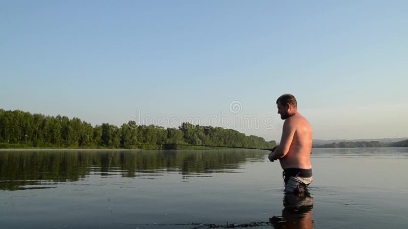 Pesca del pescador en un río tranquilo por la mañana Hombre en las artes de pesca stending en un río y tiros trole