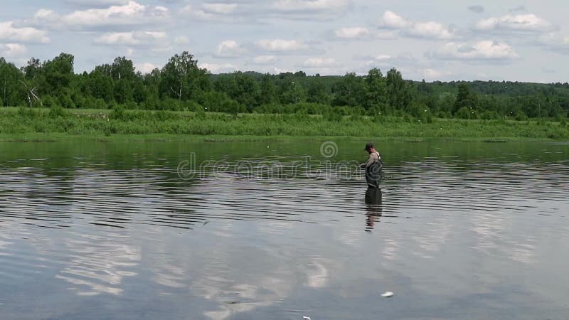 Pesca del pescador en un río tranquilo por la mañana Hombre en las artes de pesca stending en un río