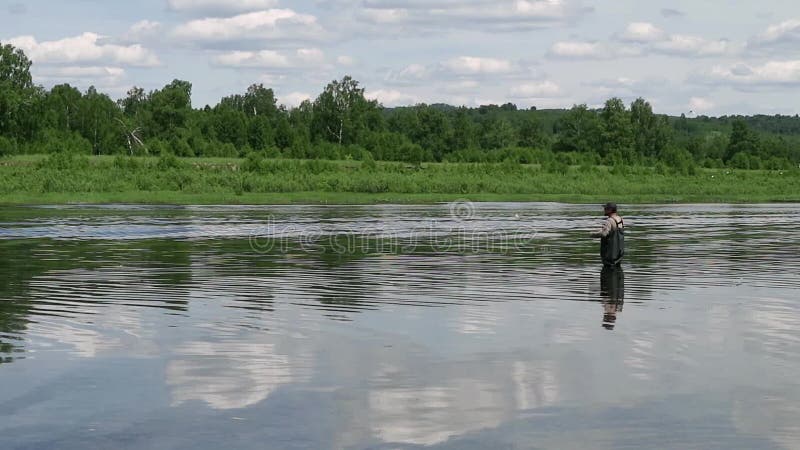 Pesca del pescador en un río tranquilo por la mañana Hombre en las artes de pesca stending en un río