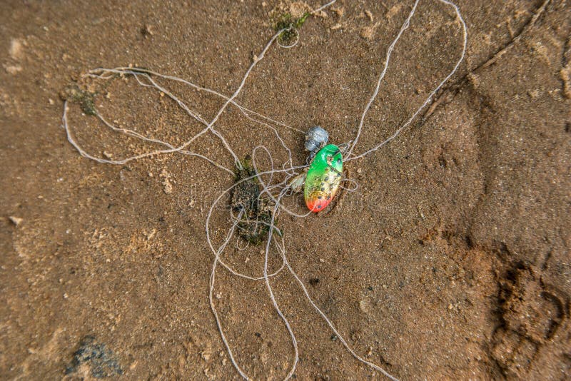 Pesca rigettata. Un esca deposto sulla spiaggia al fiume nella sabbia rigettata con un peso di piombo e un gancio sul filamento ostruito in una giornata di sole in estate