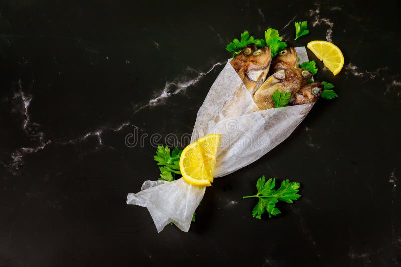 Pescado entero fresco con perejil y limón envuelto en papel pergamino sobre mesa negra fotografía de archivo libre de regalías
