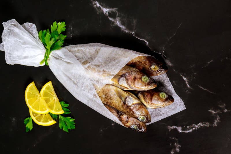 Pescado fresco y sano en pizarra negra con limón y perejil envuelto en papel pergamino imagenes de archivo