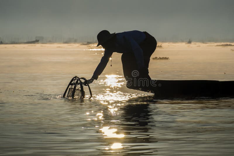 Pescador birmano en pescados de cogida del barco de bambú de la manera tradicional con la red hecha a mano fotos de archivo Pescador birmano en pescados de cogida del barco de bambú de la manera tradicional con la red hecha a mano fotos de archivo