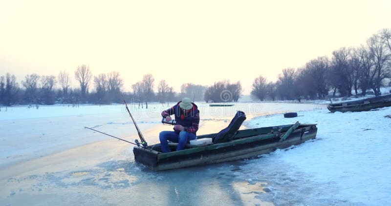Pescador pescando de un agujero en el lago desde su bote en invierno
