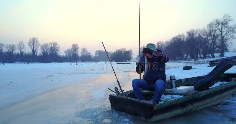Pescador pescando de un agujero en el lago desde su bote en invierno