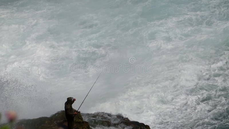 Pescador pescando en roca cerca de una gran cascada
