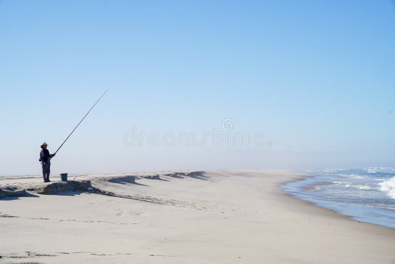 Pescador solitario en la costa namibiana larga que se coloca pacientemente que lleva a cabo el fi foto de archivo libre de regalías Pescador solitario en la costa namibiana larga que se coloca pacientemente que lleva a cabo el fi foto de archivo libre de regalías
