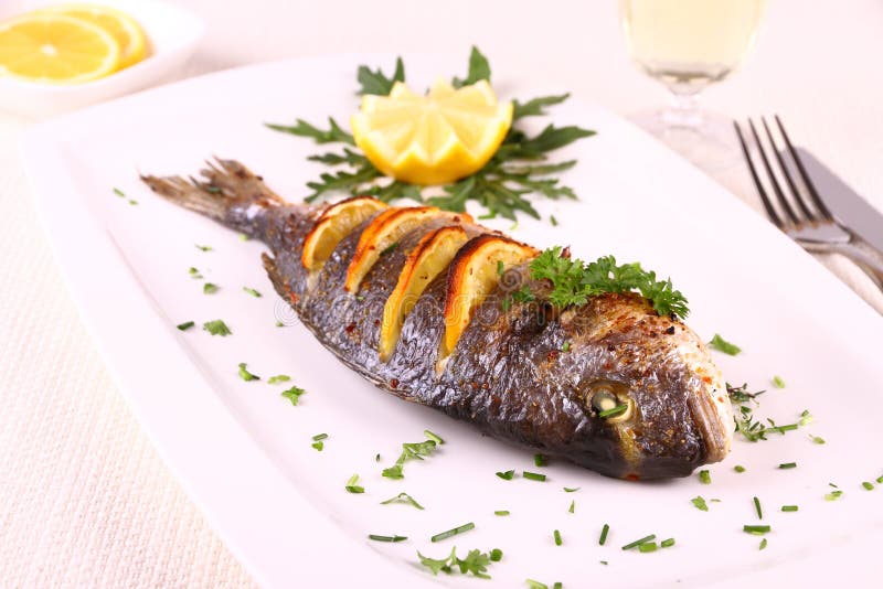 Pescados asados a la parrilla de la brema de mar, limón, arugula en la placa foto de archivo libre de regalías Pescados asados a la parrilla de la brema de mar, limón, arugula en la placa foto de archivo libre de regalías