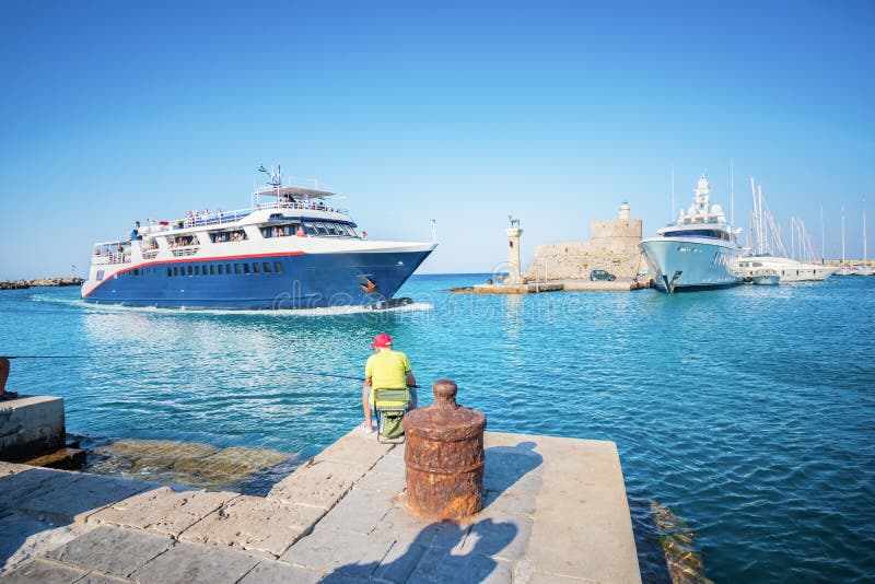 Pescatore vicino all'entrata nel porto di Mandraki in città di Rodi immagine stock libera da diritti Pescatore vicino all'entrata nel porto di Mandraki in città di Rodi immagine stock libera da diritti