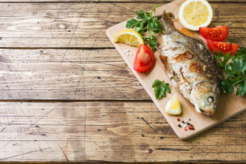 Pesce al forno della carpa con le verdure e le spezie su una tavola di legno con una copia dello spazio fotografia stock libera da diritti Pesce al forno della carpa con le verdure e le spezie su una tavola di legno con una copia dello spazio fotografia stock libera da diritti