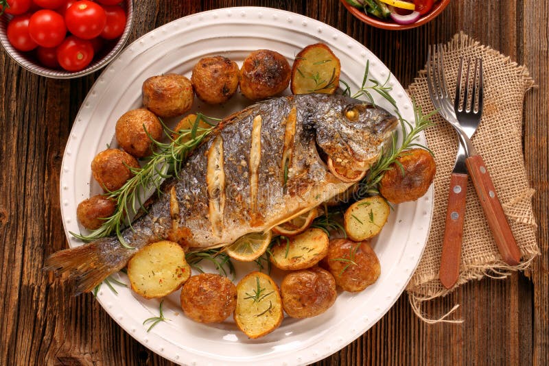 Pesce arrostito con le patate e le verdure arrostite sul piatto immagine stock Pesce arrostito con le patate e le verdure arrostite sul piatto immagine stock