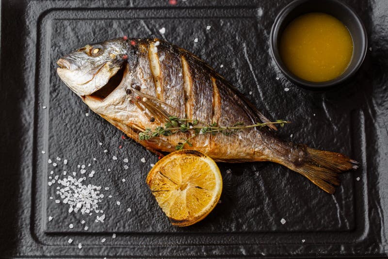 Pesce arrostito delizioso dell'orata o di dorado con le fette del limone, spezie, rosmarini sulla pietra scura Pesce di mare arro immagine stock libera da diritti Pesce arrostito delizioso dell'orata o di dorado con le fette del limone, spezie, rosmarini sulla pietra scura Pesce di mare arro immagine stock libera da diritti