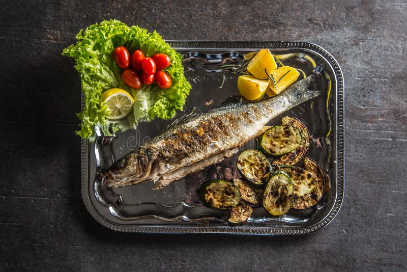 Pesce arrostito sul piatto con la verdura fresca e arrostita fotografia stock Pesce arrostito sul piatto con la verdura fresca e arrostita fotografia stock
