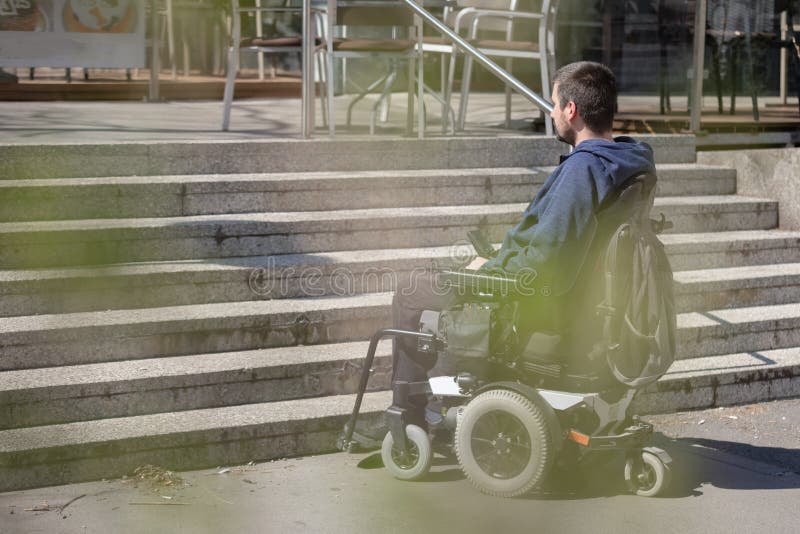 Jovem sozinho em cadeira de rodas nas escadas, problema de deficiência.  pessoas paralisadas e incapacitadas, superação de deficiências. homem  deficiente e indefeso caminhando no parque