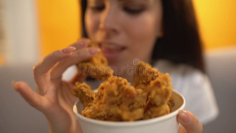 Pessoa que dá as asas de galinha roasted à menina com fome, fast food gordo delicioso