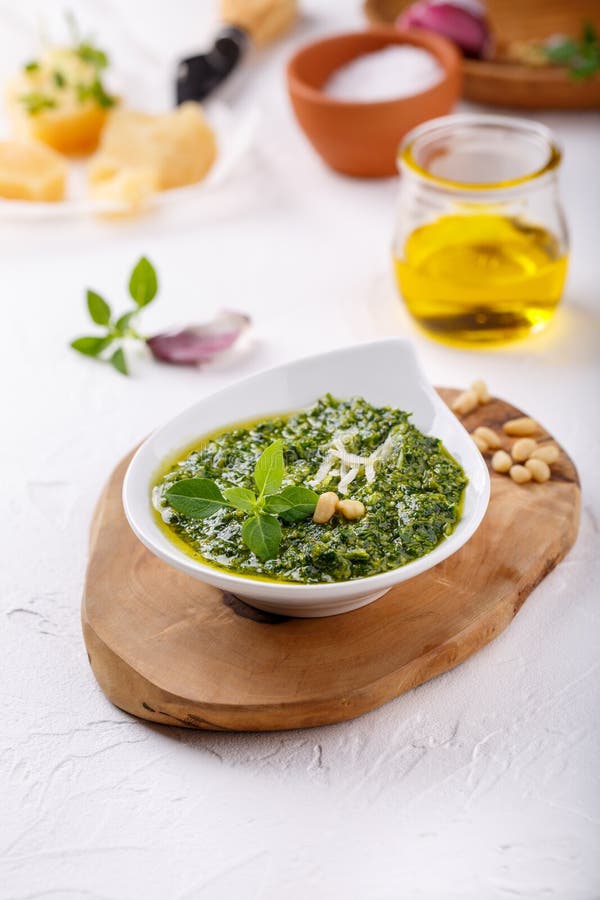 Pesto sauce with some ingredients - basil, olive oil, pine nuts, parmesan and garlic - on white table.