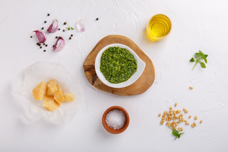 Pesto sauce with some ingredients - basil, olive oil, pine nuts, parmesan and garlic - on white table. Top view. Flat lay.