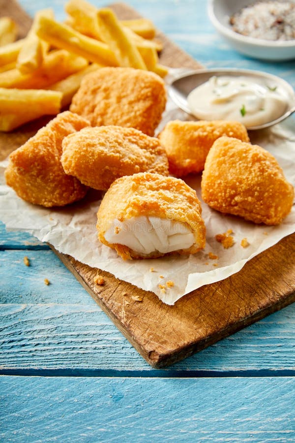 Tasty snack of fried breaded kibbeling, or bite sized portions of codfish, served on paper on a wooden board with a side dish of mayonnaise. Tasty snack of fried breaded kibbeling, or bite sized portions of codfish, served on paper on a wooden board with a side dish of mayonnaise