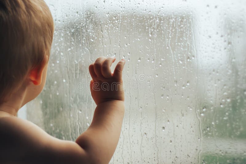 Poster Petit garçon observant la pluie par la fenêtre 