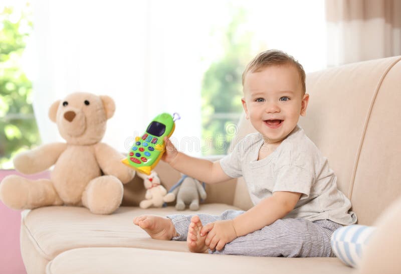 Petit bébé adorable avec le téléphone de jouet sur le sofa photos stock Petit bébé adorable avec le téléphone de jouet sur le sofa photos stock