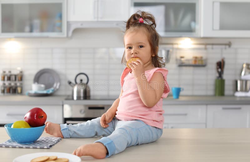 Petit bébé adorable mangeant le biscuit savoureux sur la table image stock Petit bébé adorable mangeant le biscuit savoureux sur la table image stock