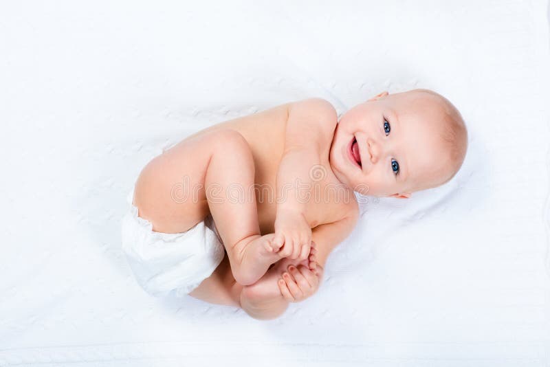 Funny little baby wearing a diaper playing on a white knitted blanket in a sunny nursery. Child after bath or shower on a fresh towel. Infant nappy change and skin care. Cute kid playing with his feet. Funny little baby wearing a diaper playing on a white knitted blanket in a sunny nursery. Child after bath or shower on a fresh towel. Infant nappy change and skin care. Cute kid playing with his feet