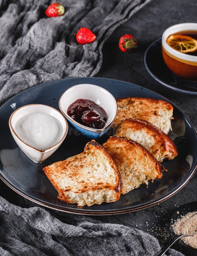 Petit d?jeuner avec les petits pains faits maison doux du plat au-dessus du fond fonc?, yaourt, confiture de fraise, une tasse de photographie stock Petit d?jeuner avec les petits pains faits maison doux du plat au-dessus du fond fonc?, yaourt, confiture de fraise, une tasse de photographie stock