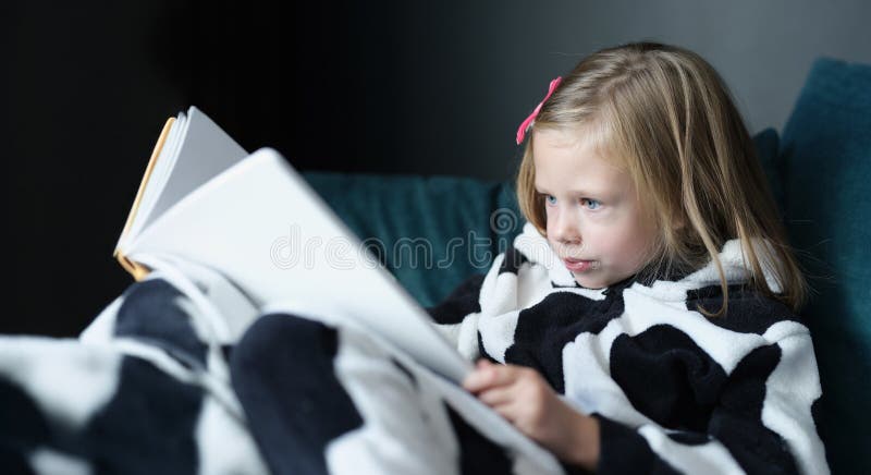 Petit enfant assis sur le canapé et le livre de lecture photographie stock