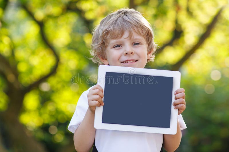 Petit enfant heureux de sourire tenant le PC de comprimé, dehors photo stock Petit enfant heureux de sourire tenant le PC de comprimé, dehors photo stock