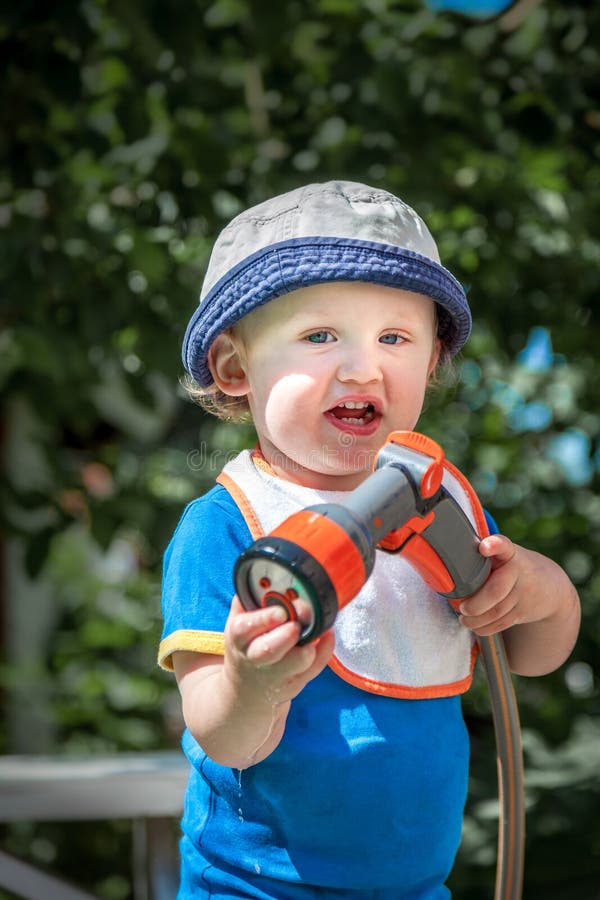 Petit enfant mignon dans le chapeau bleu tenant un jour d'été ensoleillé de tuyau d'arrosage dehors images libres de droits Petit enfant mignon dans le chapeau bleu tenant un jour d'été ensoleillé de tuyau d'arrosage dehors images libres de droits